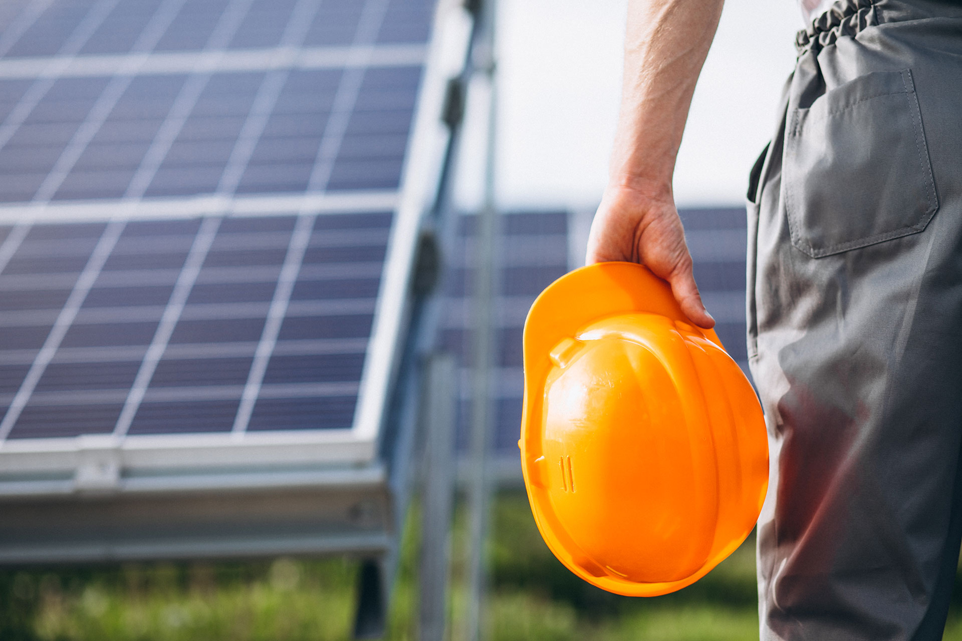Worker holding hard hat looking at large solar panels